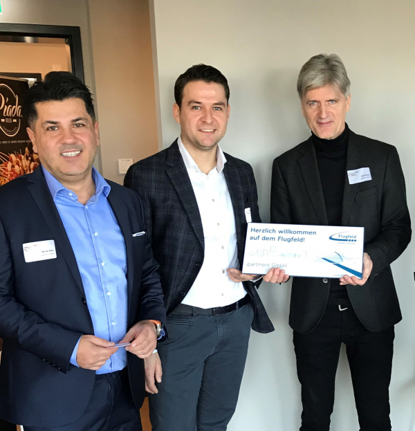 Murat Sari (Sales Manager), Markus Löwe (COO) und Ralph Stock (Geschäftsführer) von der ipartment GmbH mit dem Willkommensschild.